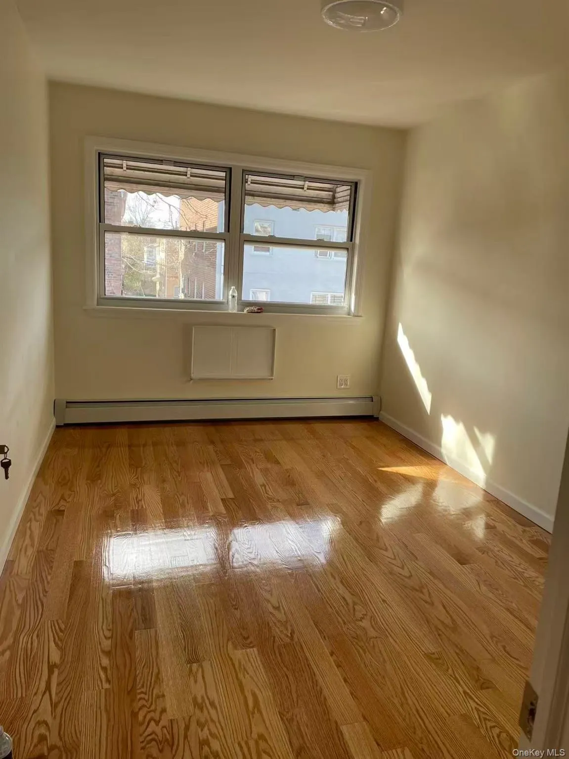 Unfurnished room with light wood finished floors and a baseboard heating unit Unfurnished room with light wood finished floors and a baseboard heating unit