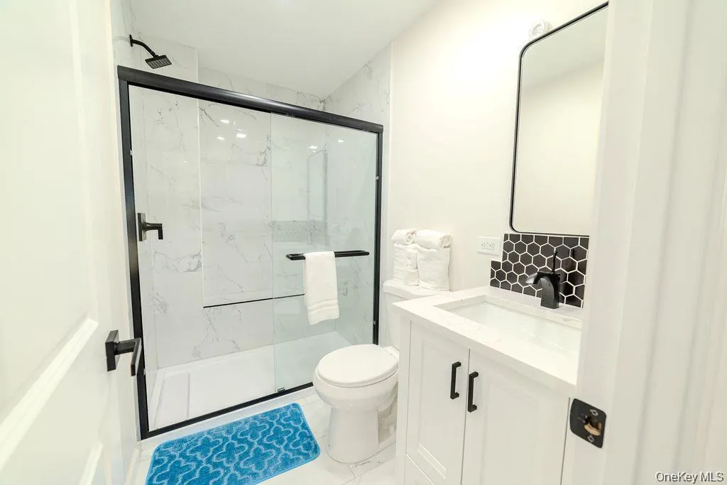 Bathroom featuring vanity, a marble finish shower, and light marble finish flooring Bathroom featuring vanity, a marble finish shower, and light marble finish flooring