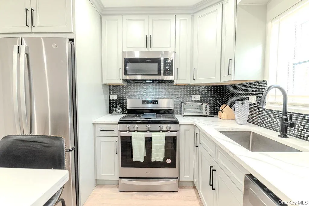 Kitchen featuring appliances with stainless steel finishes, light stone countertops, white cabinets, backsplash, and light wood finished floors Kitchen featuring appliances with stainless steel finishes, light stone countertops, white cabinets, backsplash, and light wood finished floors