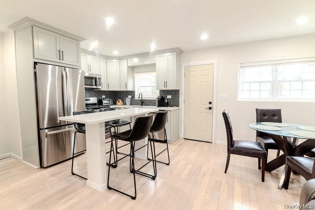 Kitchen featuring stainless steel appliances, a breakfast bar, a center island, light wood-style flooring, and white cabinets Kitchen featuring stainless steel appliances, a breakfast bar, a center island, light wood-style flooring, and white cabinets