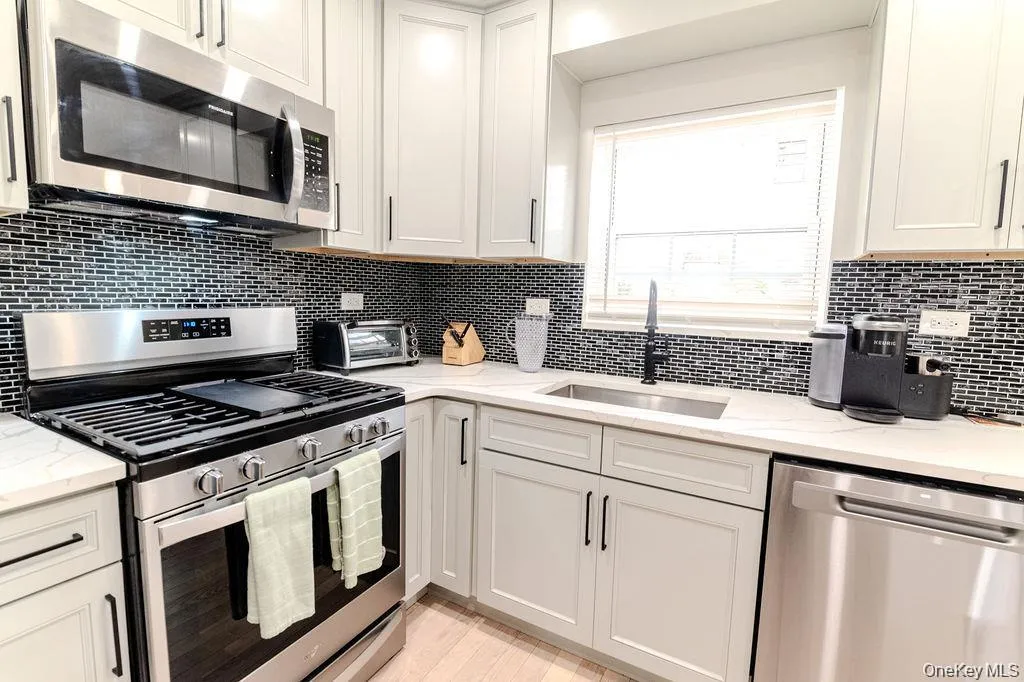 Kitchen with appliances with stainless steel finishes, light stone counters, tasteful backsplash, and white cabinets Kitchen with appliances with stainless steel finishes, light stone counters, tasteful backsplash, and white cabinets