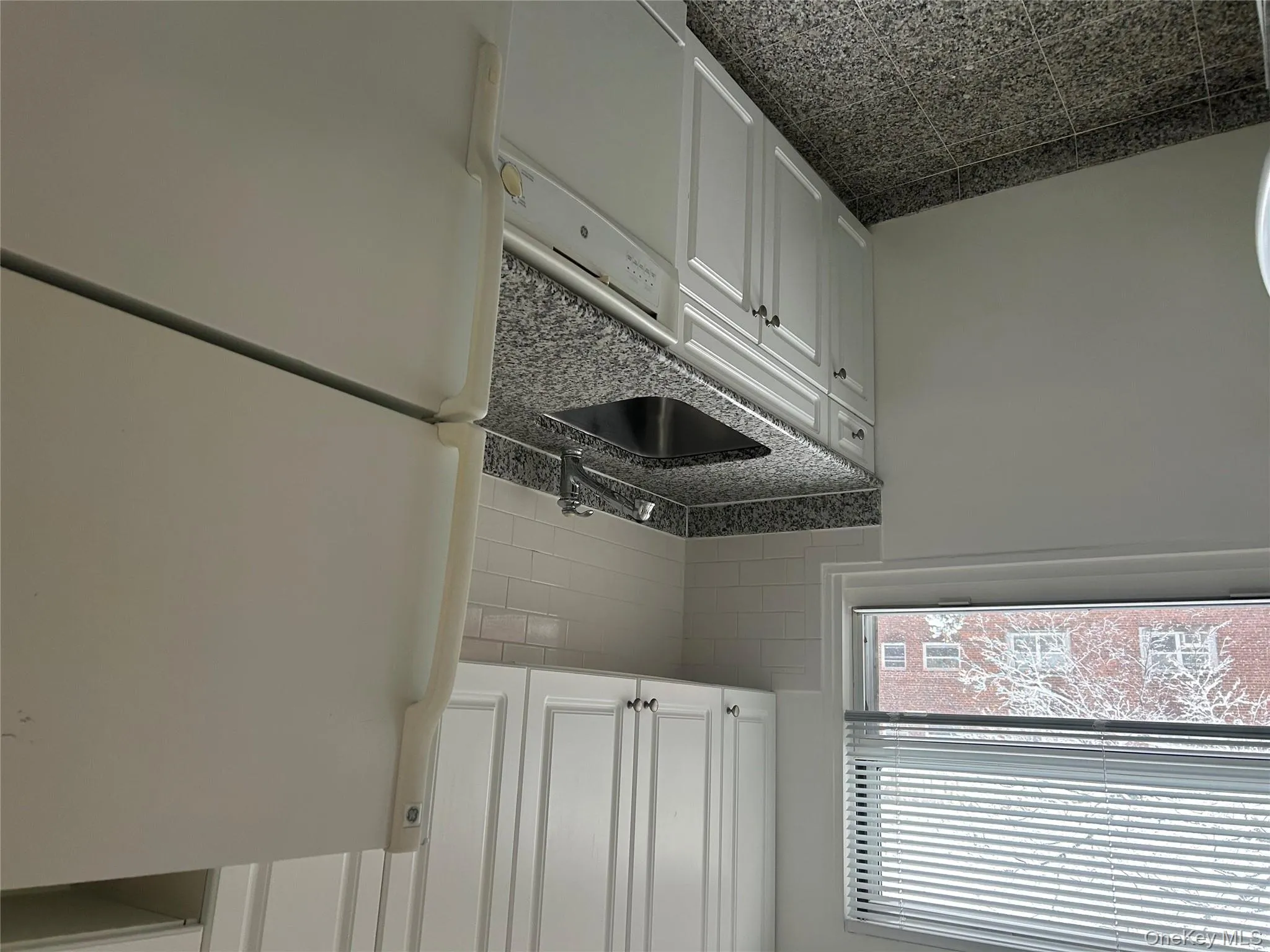 Kitchen featuring refrigerator, white cabinetry, dishwasher, dark stone counters, and decorative backsplash Kitchen featuring refrigerator, white cabinetry, dishwasher, dark stone counters, and decorative backsplash