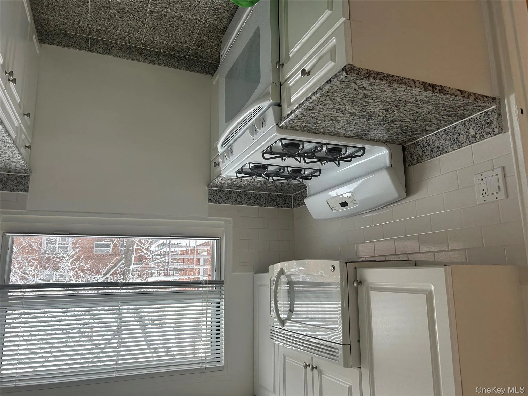 Kitchen with stove, white microwave, white cabinetry, and tasteful backsplash Kitchen with stove, white microwave, white cabinetry, and tasteful backsplash