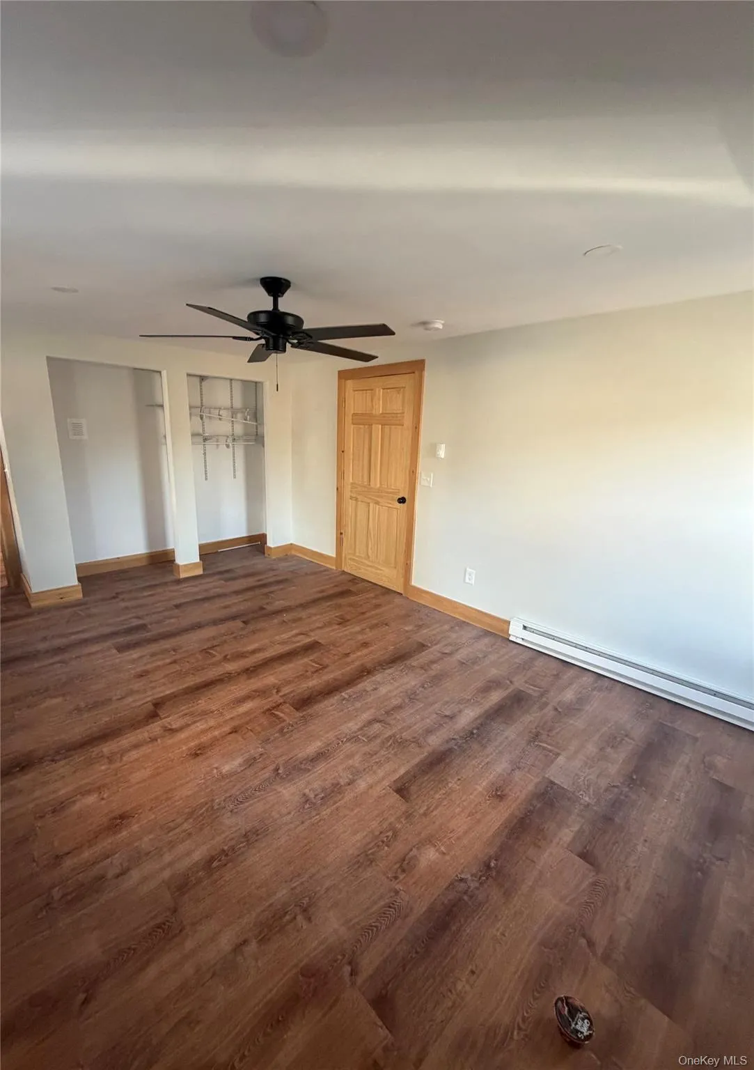 Spare room featuring baseboard heating, dark wood-style flooring, and ceiling fan Spare room featuring baseboard heating, dark wood-style flooring, and ceiling fan