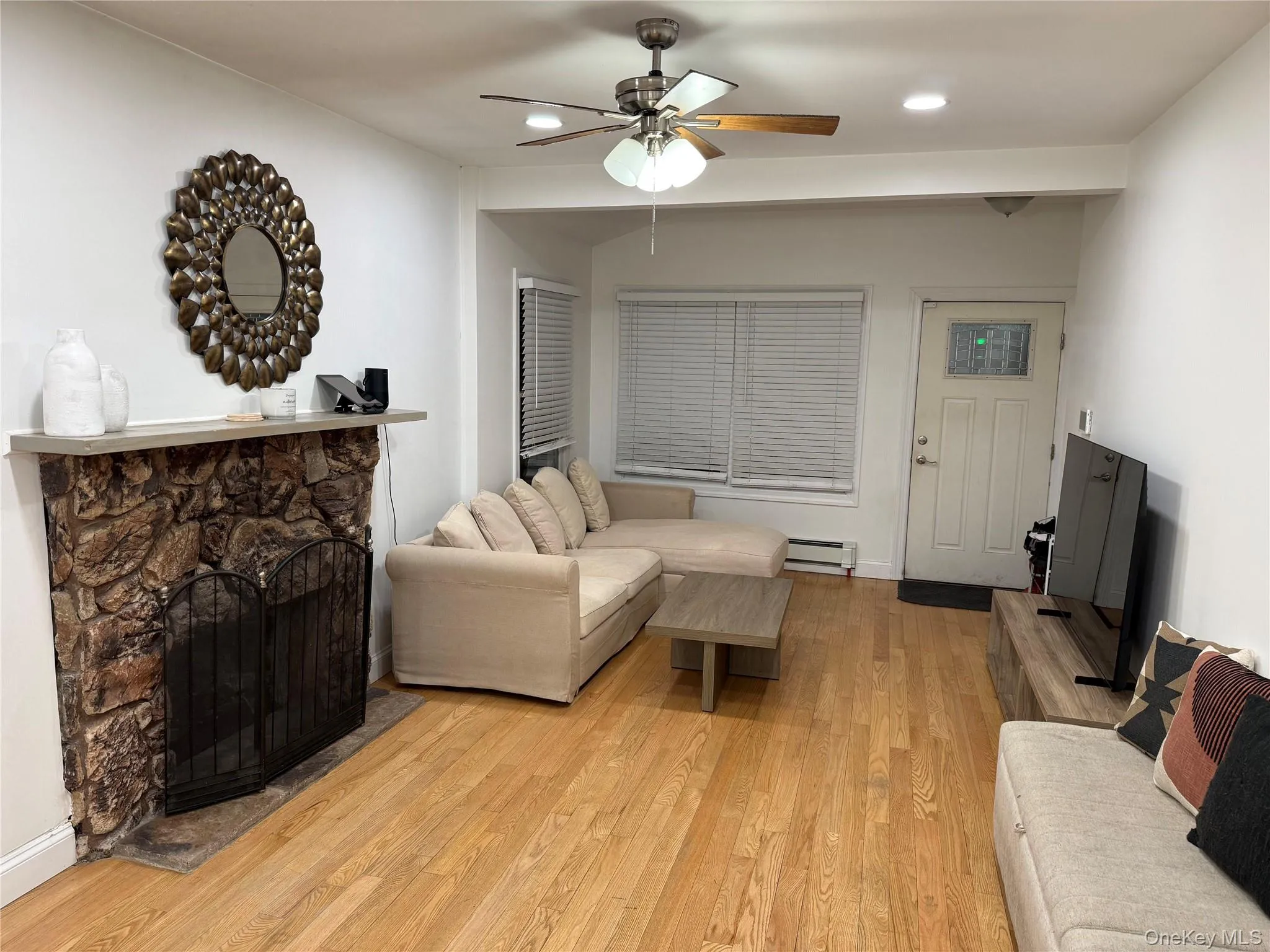 Living area with a fireplace, light wood-type flooring, recessed lighting, a ceiling fan, and a baseboard radiator Living area with a fireplace, light wood-type flooring, recessed lighting, a ceiling fan, and a baseboard radiator
