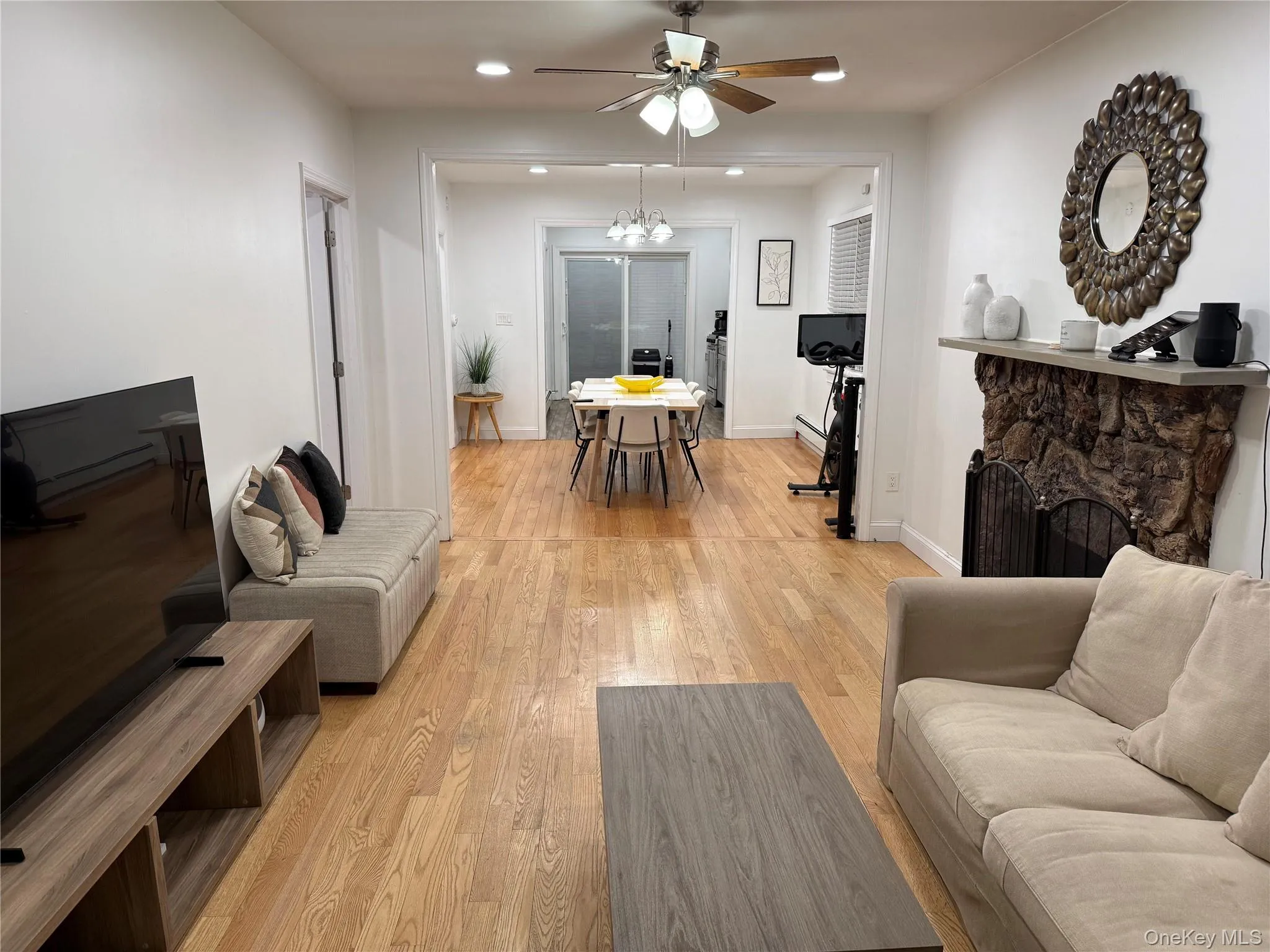 Living area featuring a stone fireplace, light wood-style floors, recessed lighting, ceiling fan, and a chandelier Living area featuring a stone fireplace, light wood-style floors, recessed lighting, ceiling fan, and a chandelier