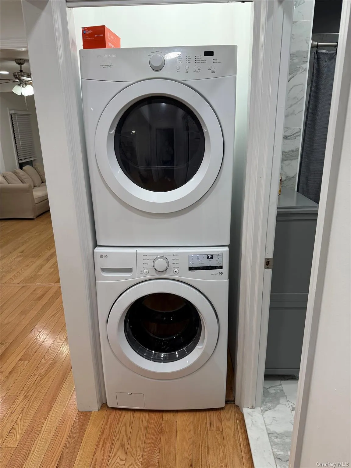 Laundry room with stacked washing machine and dryer, light wood-style flooring, and a ceiling fan Laundry room with stacked washing machine and dryer, light wood-style flooring, and a ceiling fan