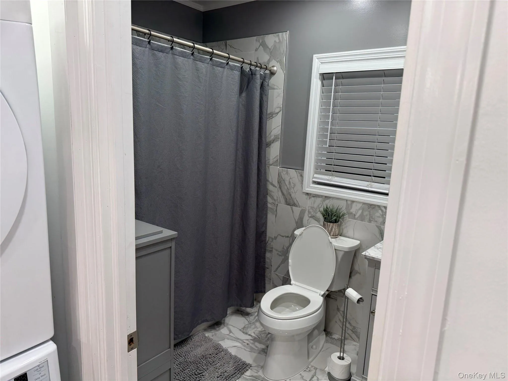 Bathroom featuring a shower with curtain, tile walls, marble look tile flooring, vanity, and a wainscoted wall Bathroom featuring a shower with curtain, tile walls, marble look tile flooring, vanity, and a wainscoted wall