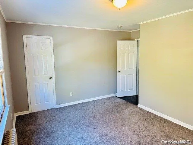 Unfurnished room featuring dark colored carpet, ornamental molding, and radiator heating unit Unfurnished room featuring dark colored carpet, ornamental molding, and radiator heating unit