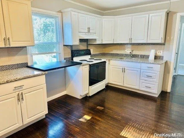 Kitchen with white cabinetry, white electric range, dark wood-style flooring, under cabinet range hood, and ornamental molding Kitchen with white cabinetry, white electric range, dark wood-style flooring, under cabinet range hood, and ornamental molding