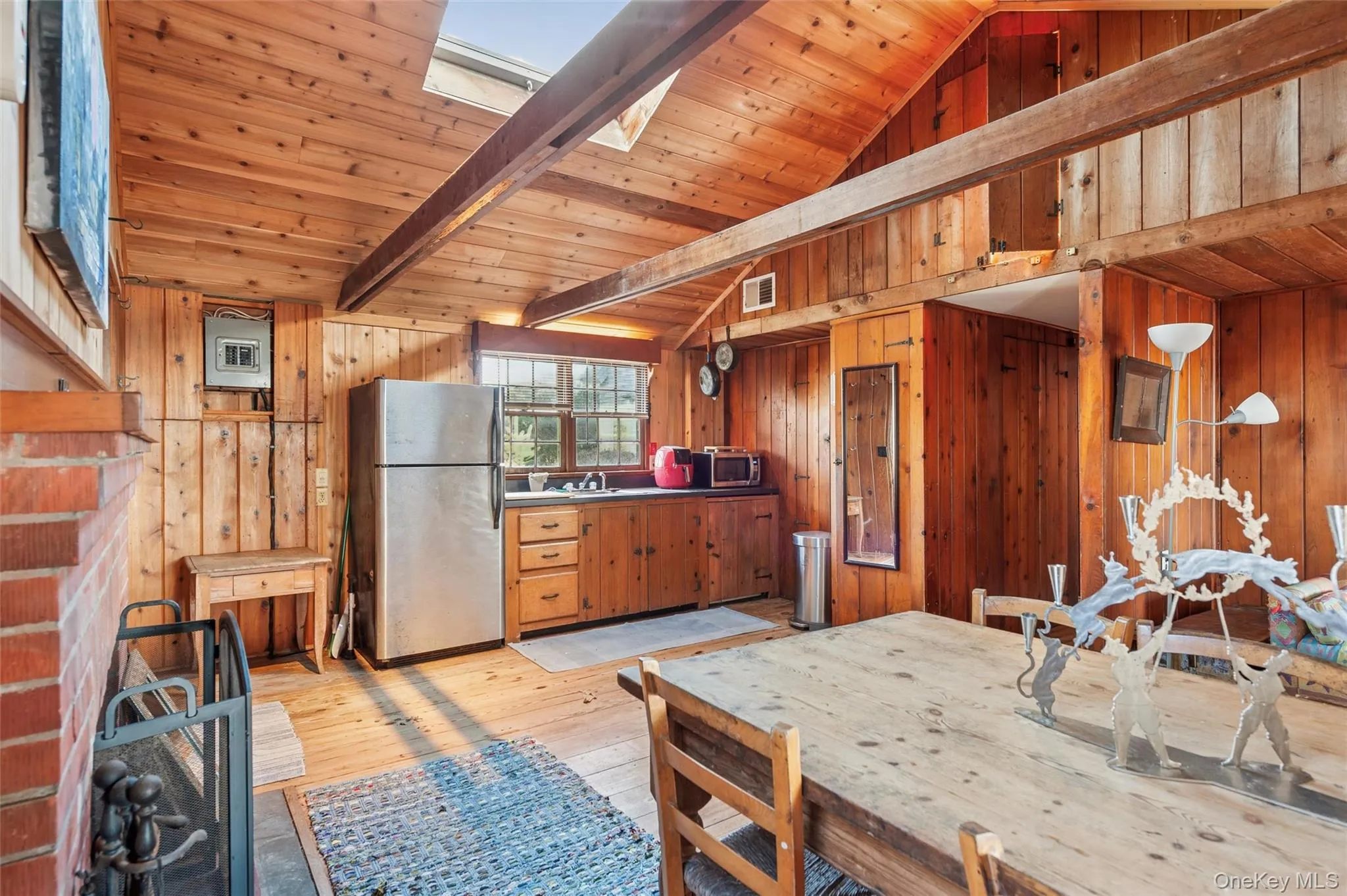 Kitchen featuring stainless steel appliances, light wood-style floors, wood ceiling, wood walls, and brown cabinetry Kitchen featuring stainless steel appliances, light wood-style floors, wood ceiling, wood walls, and brown cabinetry