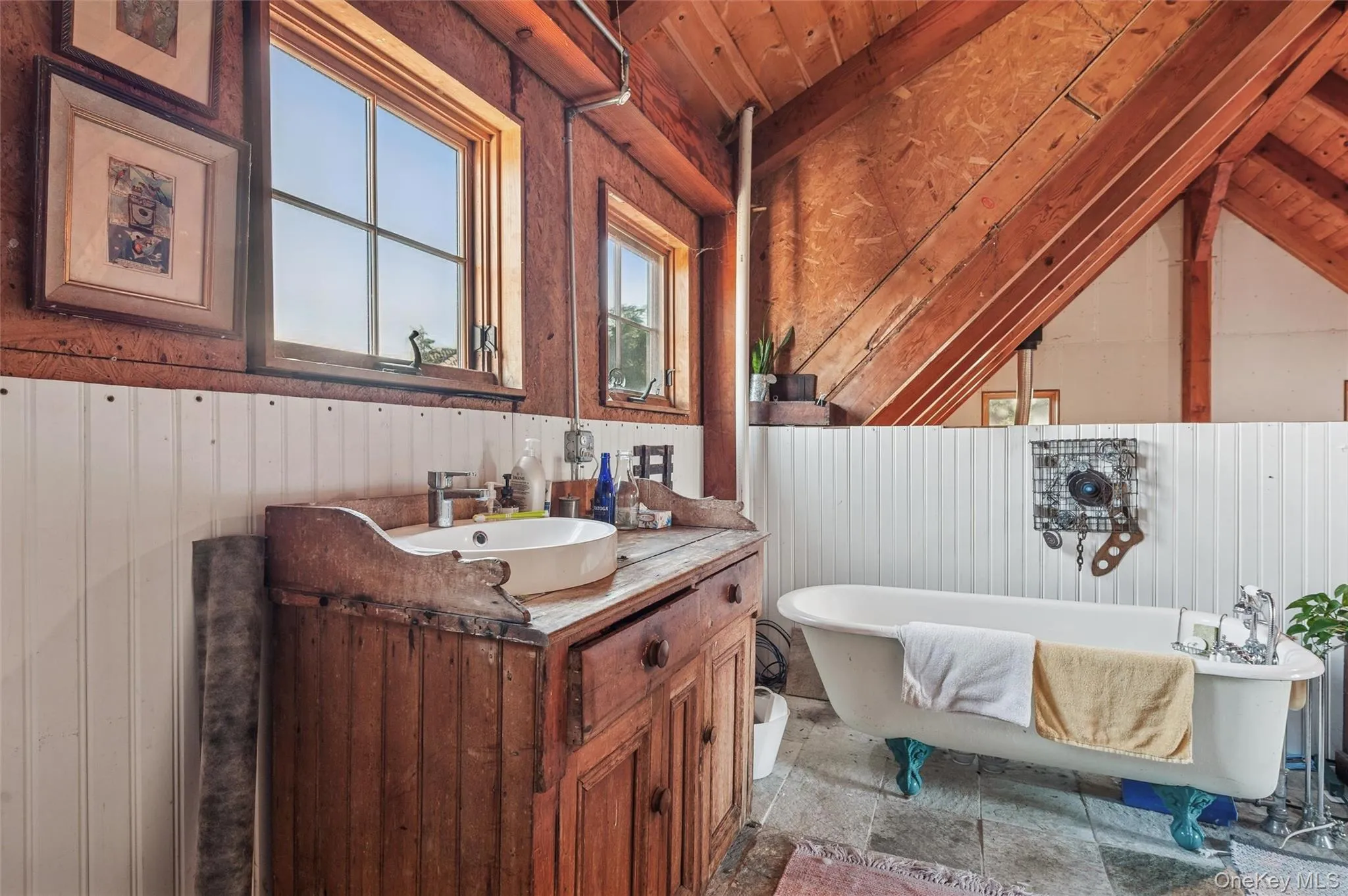 Bathroom featuring a freestanding bath, vanity, lofted ceiling, wood walls, and stone tile flooring Bathroom featuring a freestanding bath, vanity, lofted ceiling, wood walls, and stone tile flooring