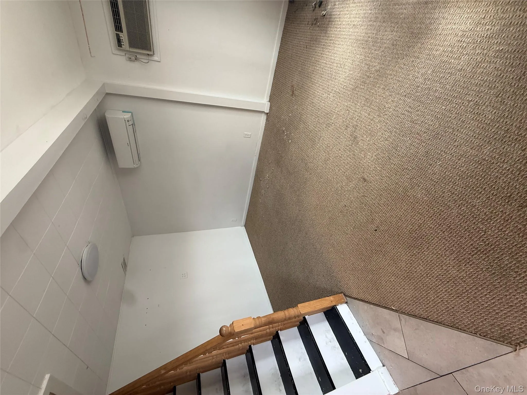 Finished below grade area featuring light colored carpet, a wall mounted air conditioner, and stairs Finished below grade area featuring light colored carpet, a wall mounted air conditioner, and stairs