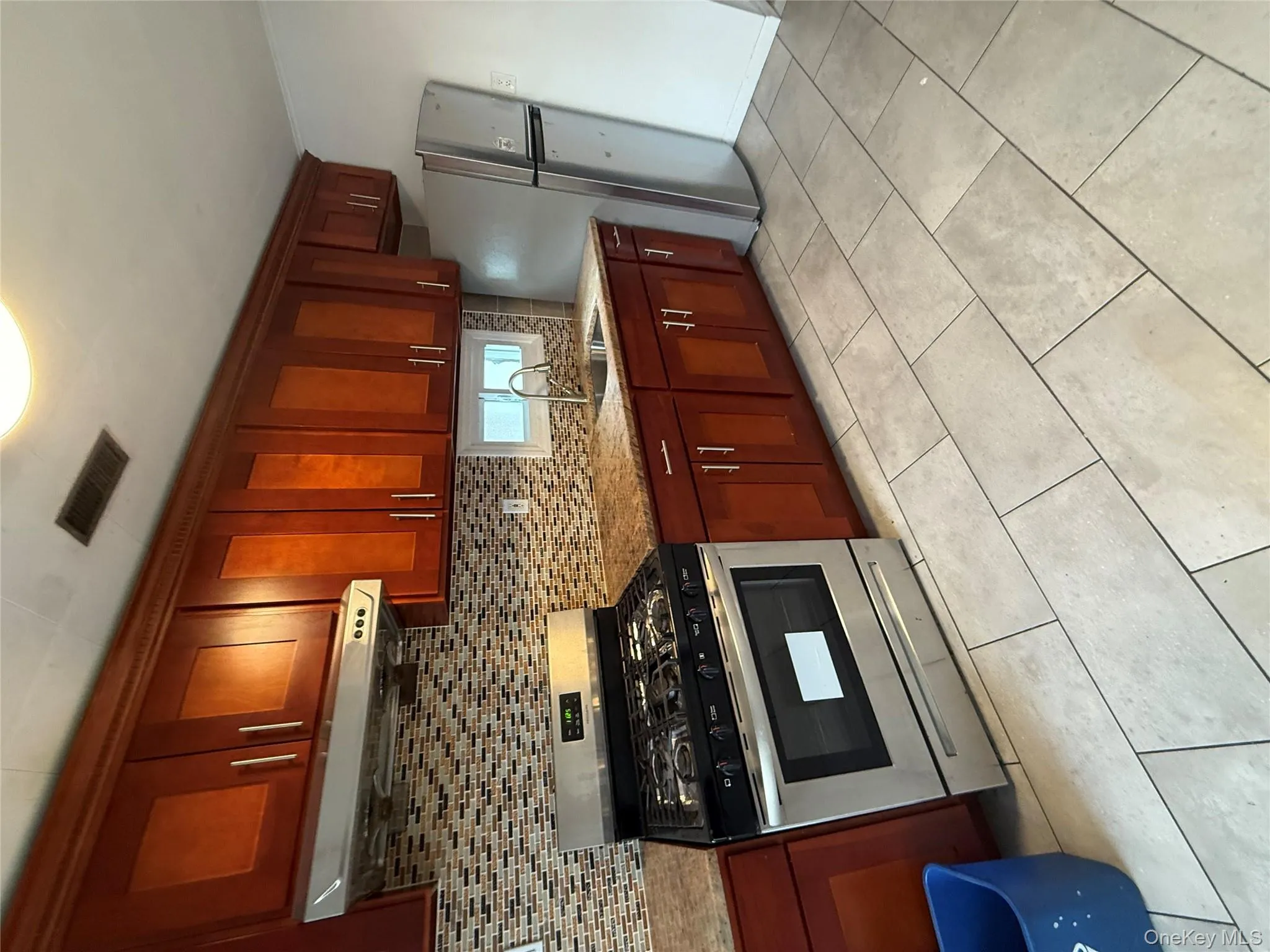 Kitchen with stainless steel range, refrigerator, ventilation hood, backsplash, and reddish brown cabinets Kitchen with stainless steel range, refrigerator, ventilation hood, backsplash, and reddish brown cabinets