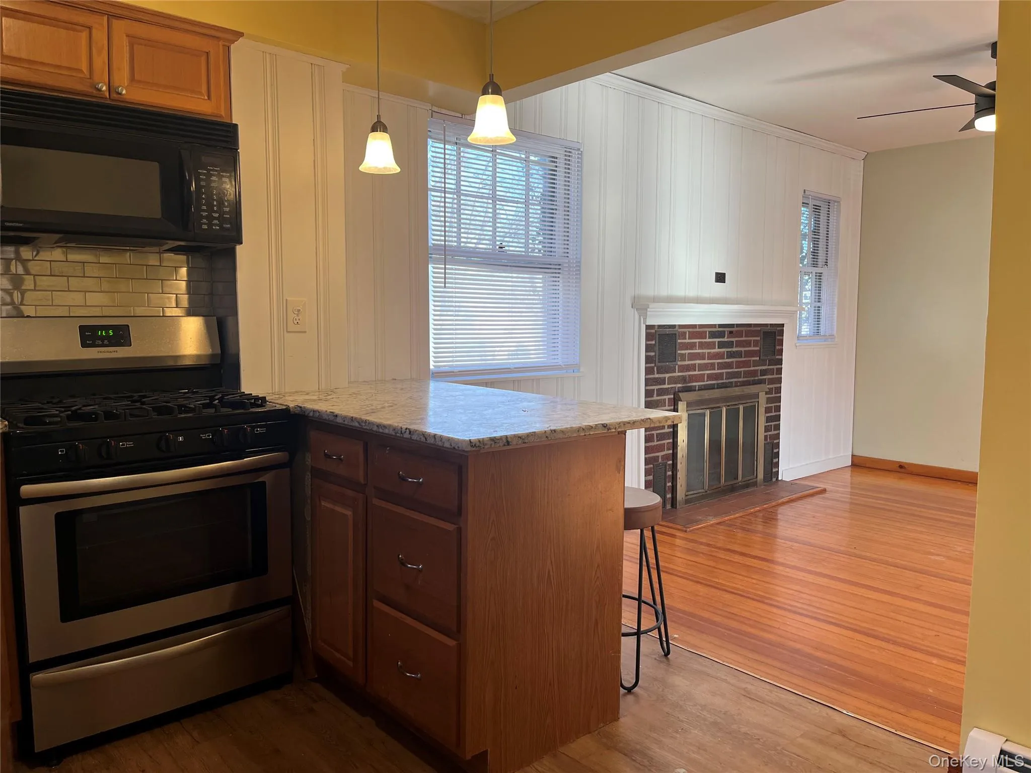 Kitchen featuring stainless steel gas stove, black microwave, light wood-style floors, a breakfast bar, and a fireplace Kitchen featuring stainless steel gas stove, black microwave, light wood-style floors, a breakfast bar, and a fireplace