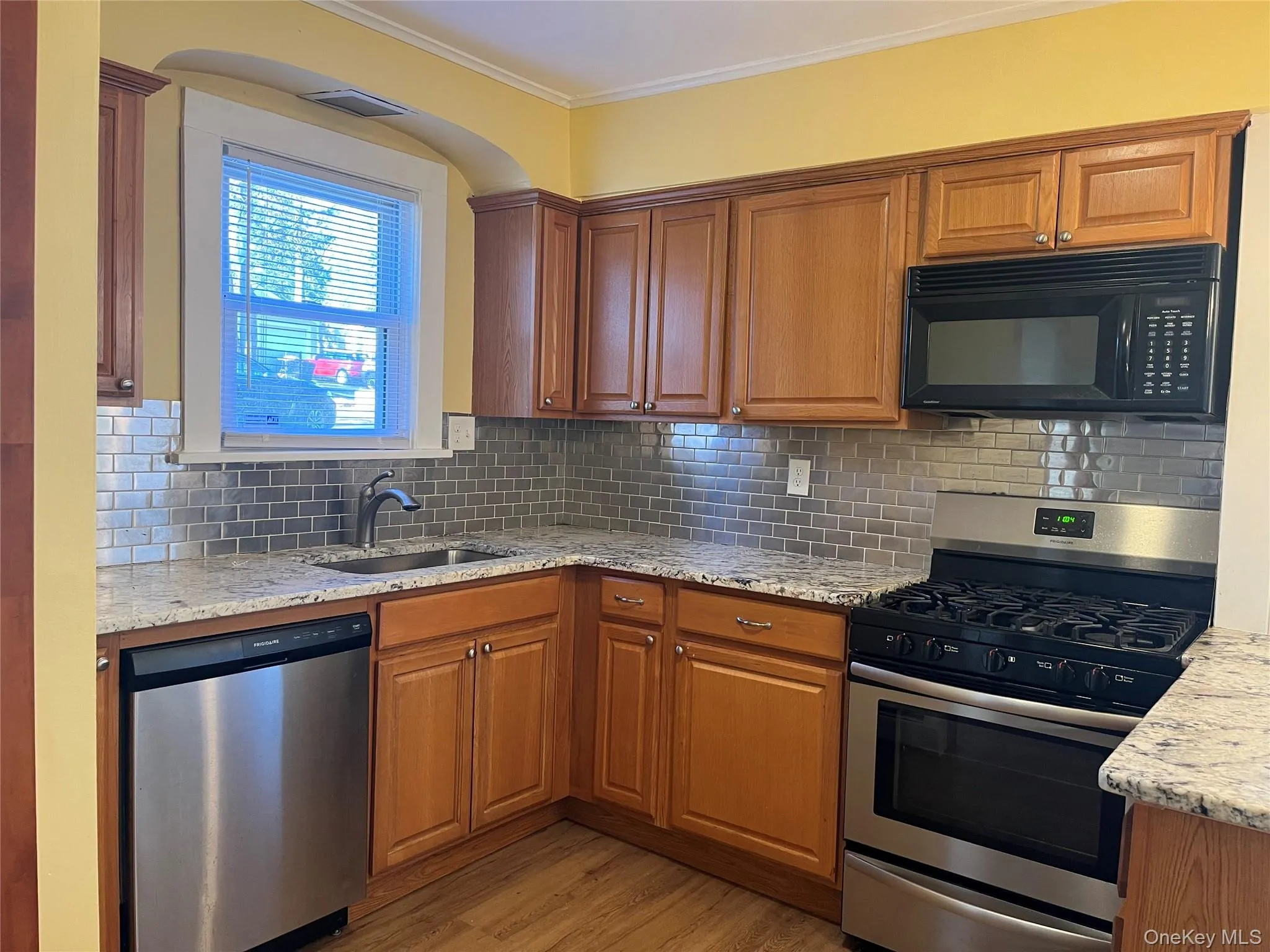 Kitchen featuring stainless steel appliances, light stone countertops, and brown cabinetry Kitchen featuring stainless steel appliances, light stone countertops, and brown cabinetry