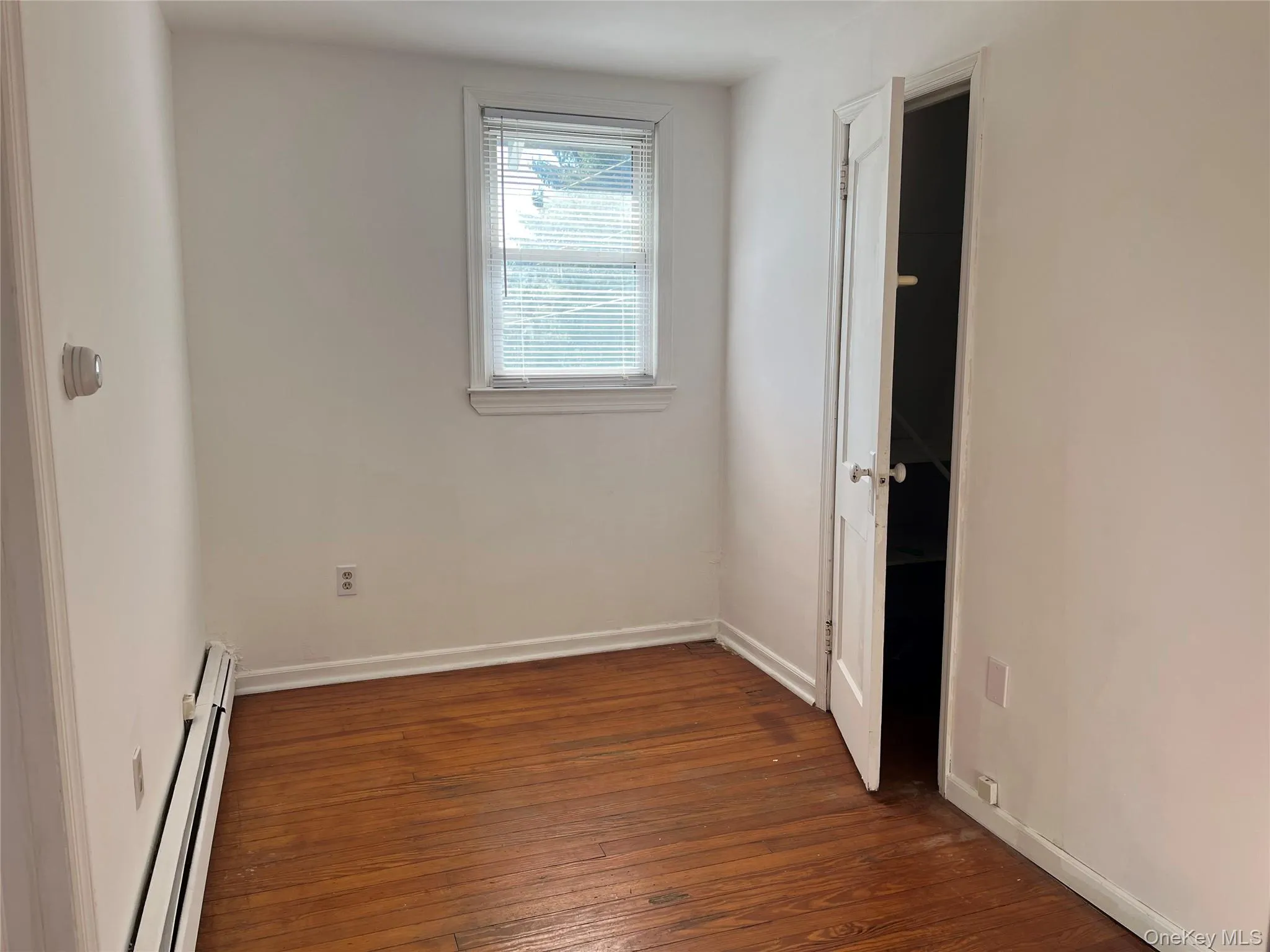 Empty room with a baseboard radiator and dark wood-style floors Empty room with a baseboard radiator and dark wood-style floors