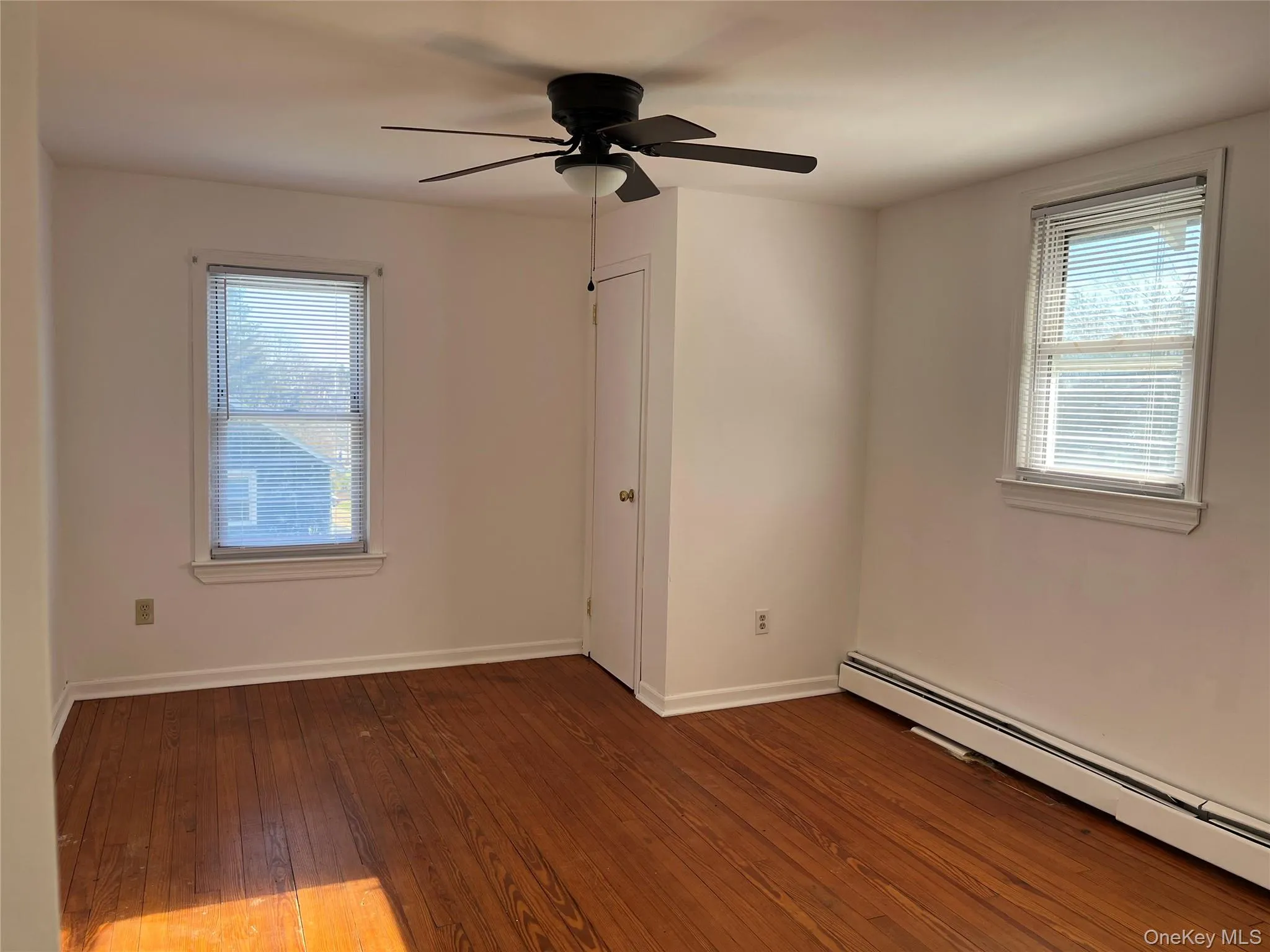 Spare room with a baseboard radiator, dark wood-style floors, plenty of natural light, and a ceiling fan Spare room with a baseboard radiator, dark wood-style floors, plenty of natural light, and a ceiling fan