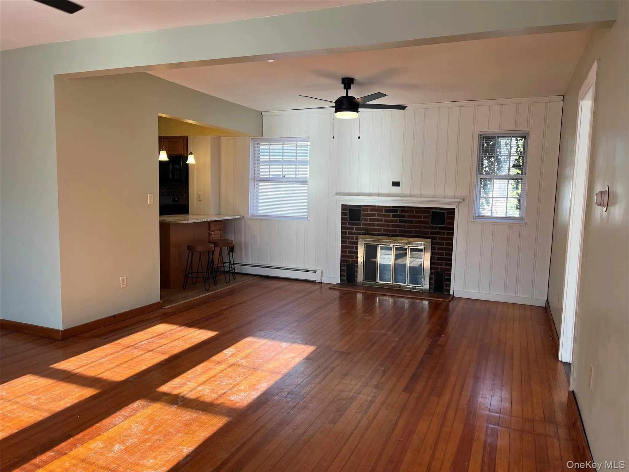 Unfurnished living room featuring a ceiling fan, a fireplace, dark wood-style floors, and a baseboard heating unit Unfurnished living room featuring a ceiling fan, a fireplace, dark wood-style floors, and a baseboard heating unit