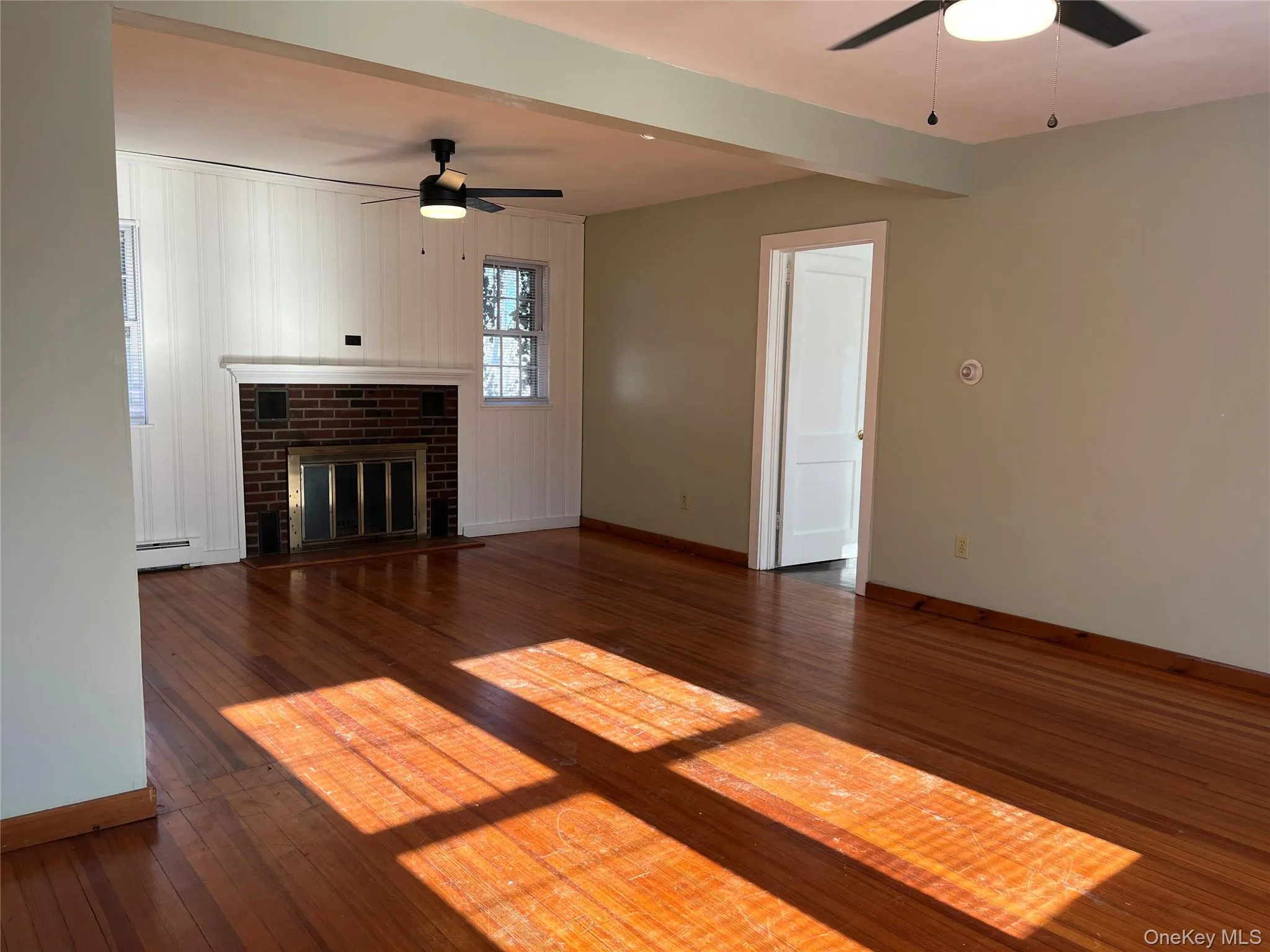 Unfurnished living room featuring ceiling fan, a fireplace, dark wood-type flooring, a baseboard heating unit, and beam ceiling Unfurnished living room featuring ceiling fan, a fireplace, dark wood-type flooring, a baseboard heating unit, and beam ceiling