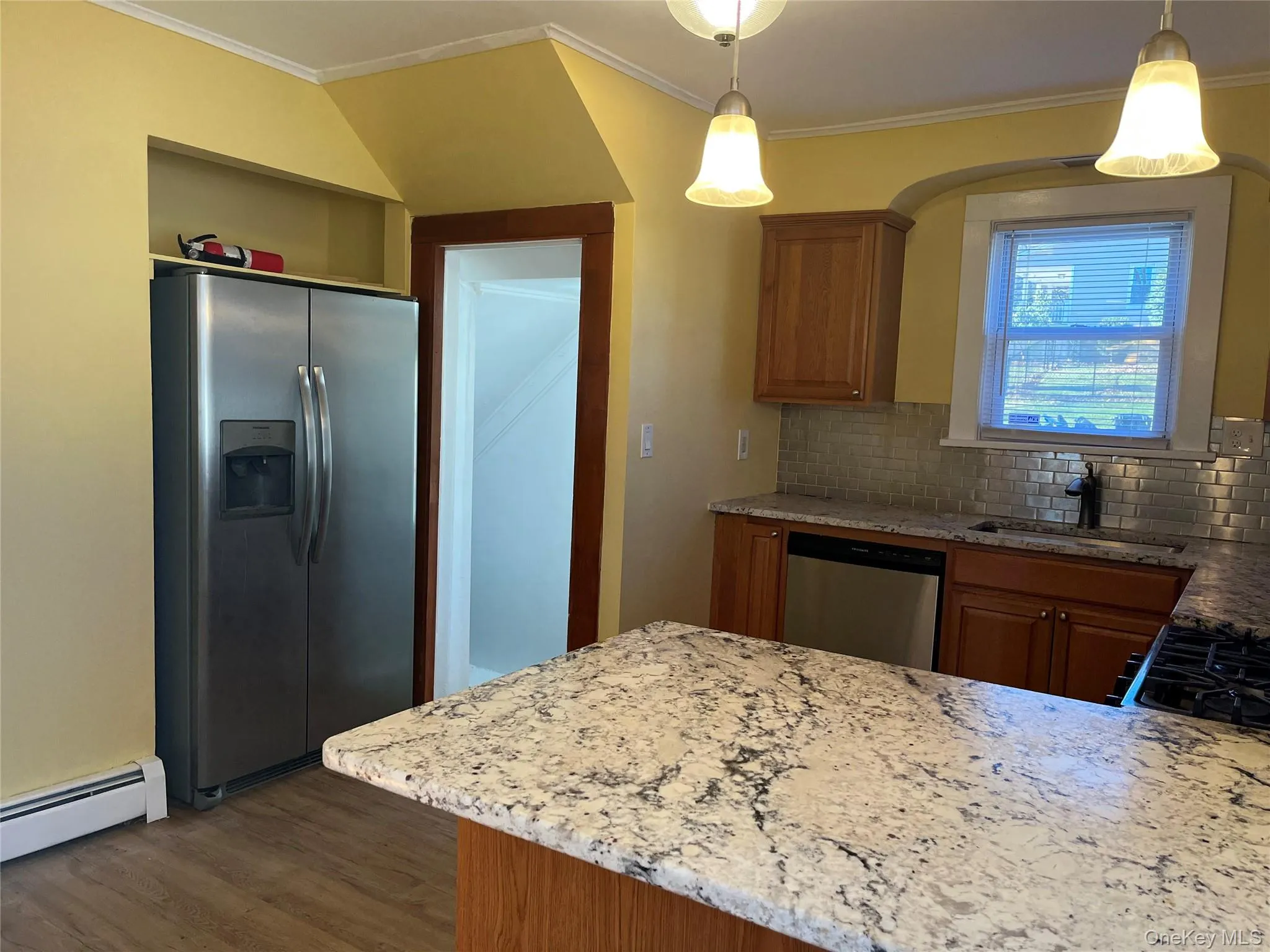 Kitchen featuring light stone countertops, stainless steel appliances, brown cabinetry, crown molding, and backsplash Kitchen featuring light stone countertops, stainless steel appliances, brown cabinetry, crown molding, and backsplash