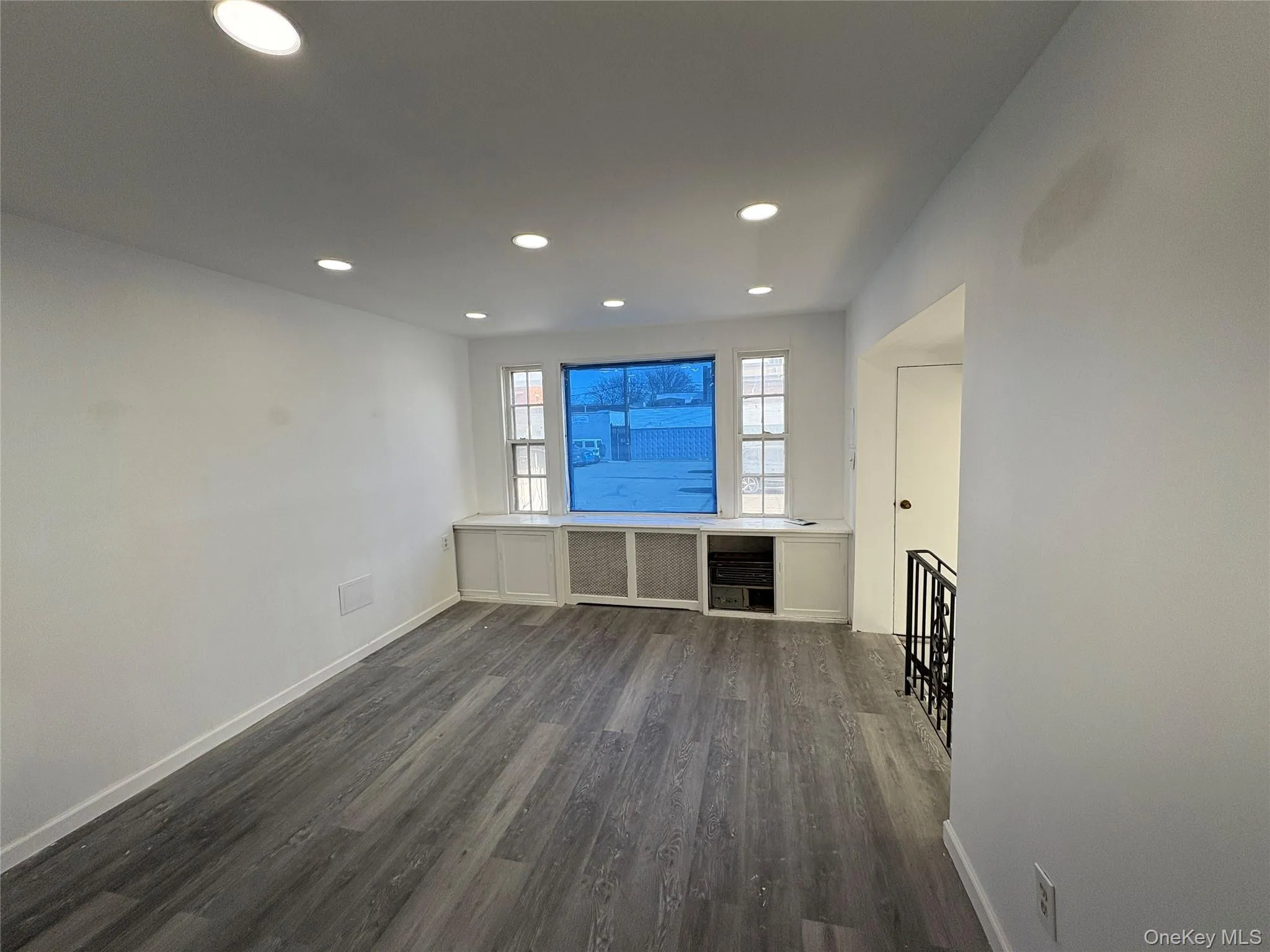 Unfurnished living room featuring dark wood-style flooring, recessed lighting, and radiator heating unit Unfurnished living room featuring dark wood-style flooring, recessed lighting, and radiator heating unit