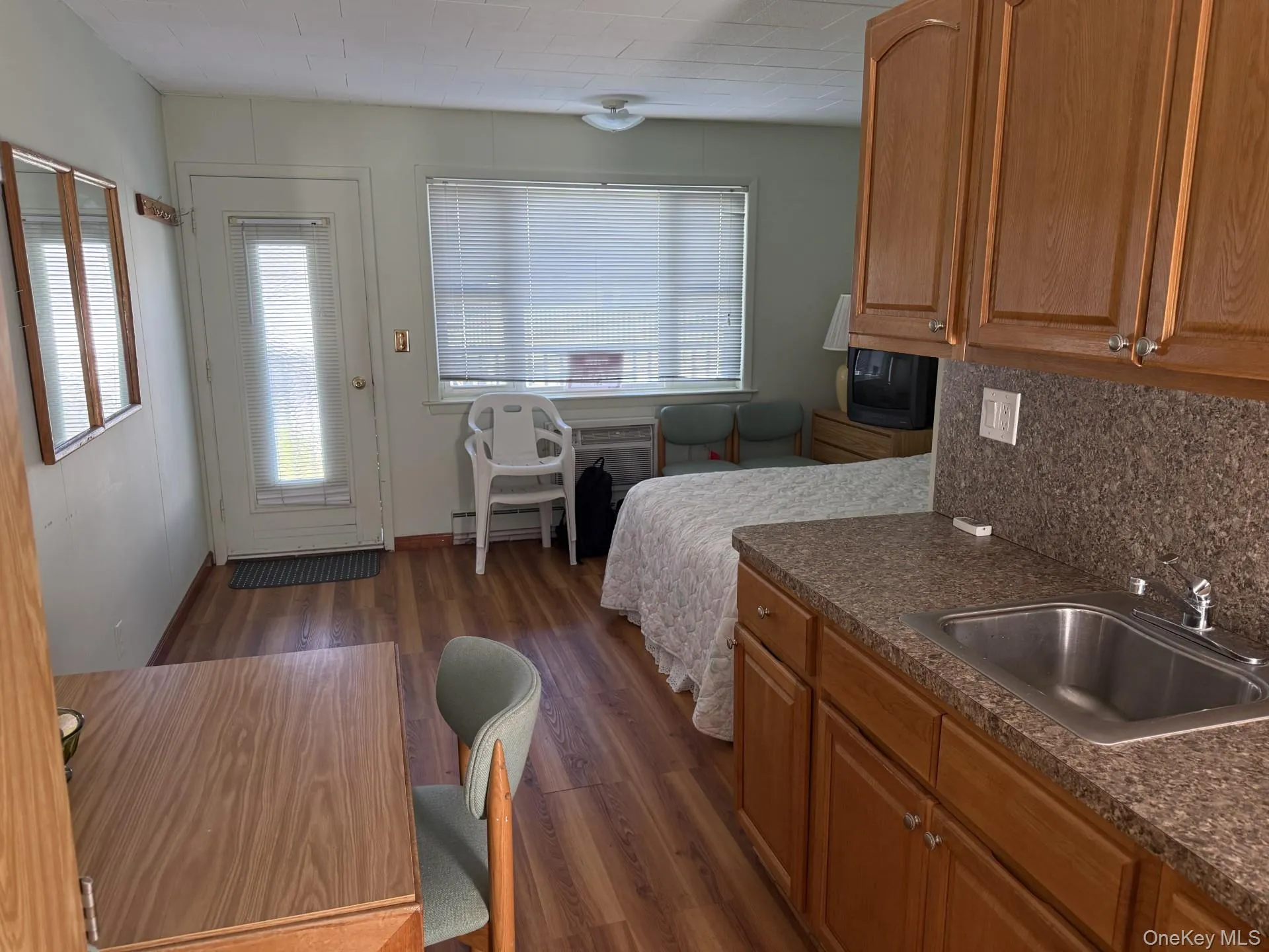 Kitchen featuring dark countertops, dark wood-style flooring, brown cabinets, baseboard heating, and tasteful backsplash Kitchen featuring dark countertops, dark wood-style flooring, brown cabinets, baseboard heating, and tasteful backsplash