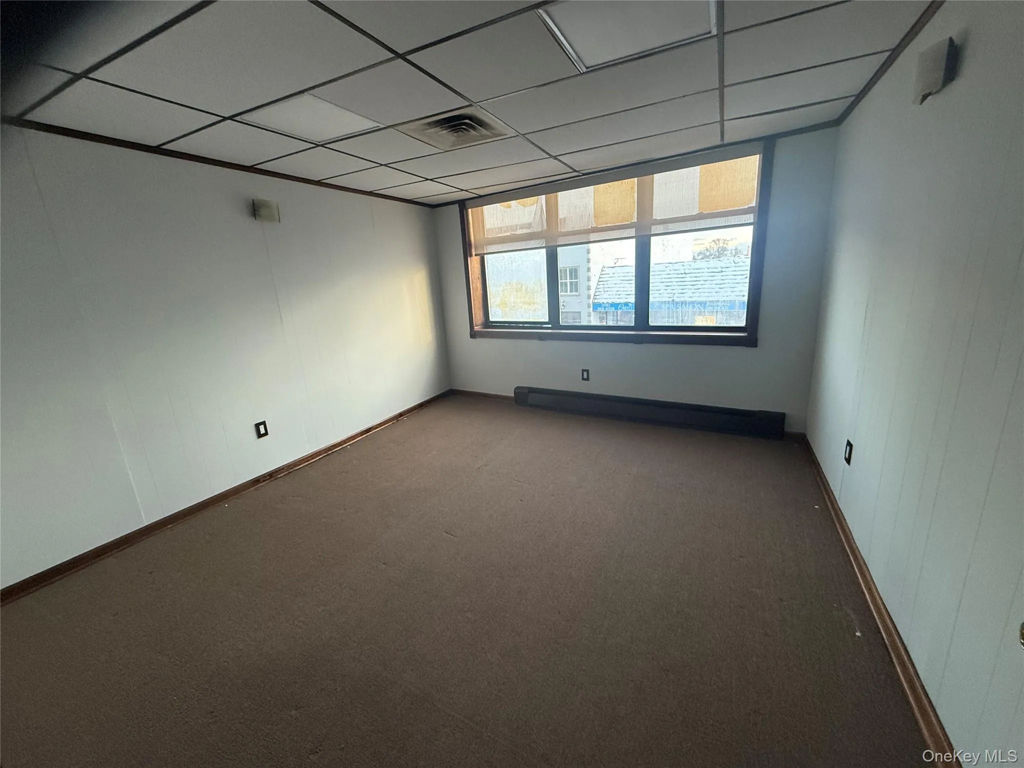 Empty room featuring carpet flooring, a drop ceiling, and a baseboard radiator Empty room featuring carpet flooring, a drop ceiling, and a baseboard radiator