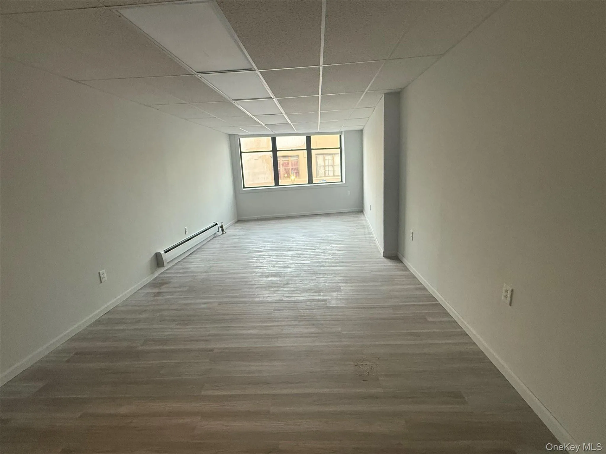 Unfurnished room with a paneled ceiling, wood finished floors, and a baseboard heating unit Unfurnished room with a paneled ceiling, wood finished floors, and a baseboard heating unit