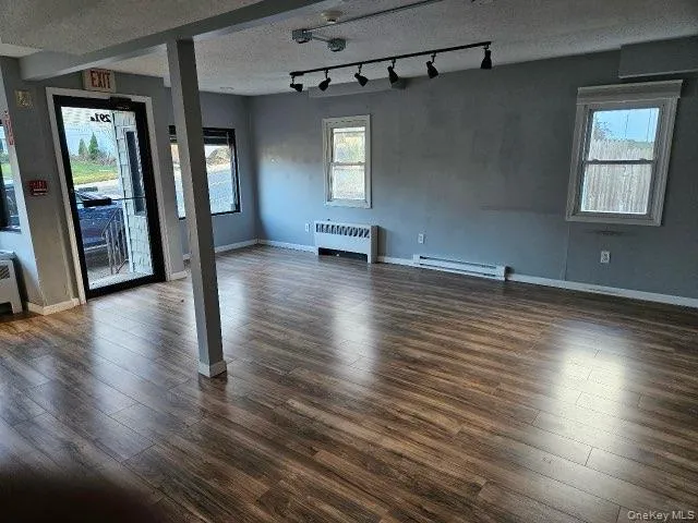 Unfurnished living room with track lighting, dark wood-style floors, radiator, healthy amount of natural light, and a textured ceiling Unfurnished living room with track lighting, dark wood-style floors, radiator, healthy amount of natural light, and a textured ceiling