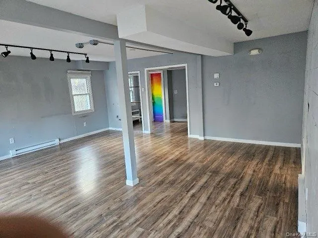 Empty room featuring track lighting, baseboard heating, and dark wood finished floors Empty room featuring track lighting, baseboard heating, and dark wood finished floors