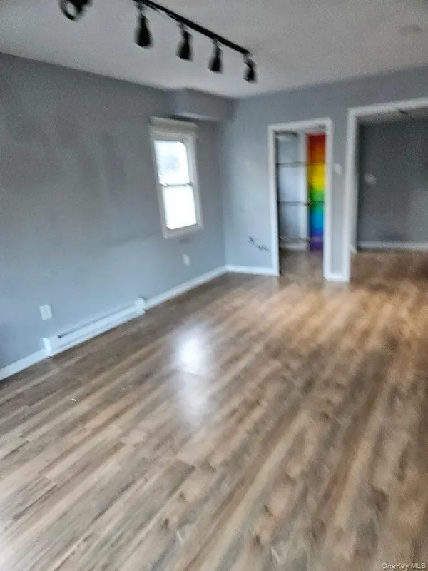 Unfurnished bedroom featuring track lighting, a baseboard heating unit, and wood finished floors Unfurnished bedroom featuring track lighting, a baseboard heating unit, and wood finished floors