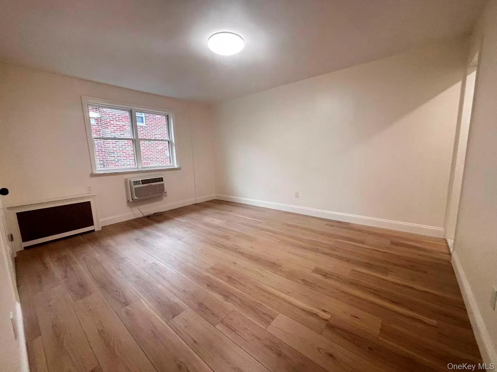 Empty room with light wood-type flooring, radiator heating unit, and an AC wall unit Empty room with light wood-type flooring, radiator heating unit, and an AC wall unit