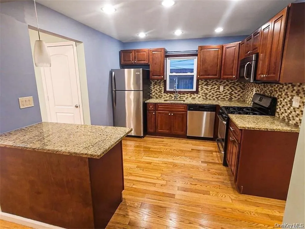 Kitchen with appliances with stainless steel finishes, light stone countertops, pendant lighting, light wood-style flooring, and recessed lighting Kitchen with appliances with stainless steel finishes, light stone countertops, pendant lighting, light wood-style flooring, and recessed lighting