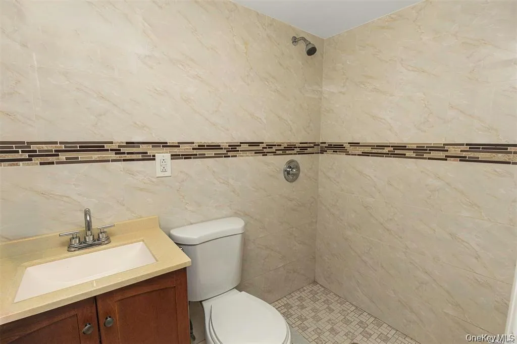 Bathroom featuring a shower stall, vanity, and tile walls Bathroom featuring a shower stall, vanity, and tile walls