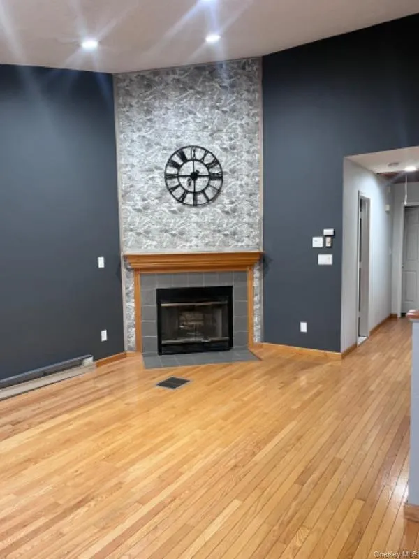 Unfurnished living room with light wood finished floors, a tiled fireplace, recessed lighting, and a baseboard radiator Unfurnished living room with light wood finished floors, a tiled fireplace, recessed lighting, and a baseboard radiator