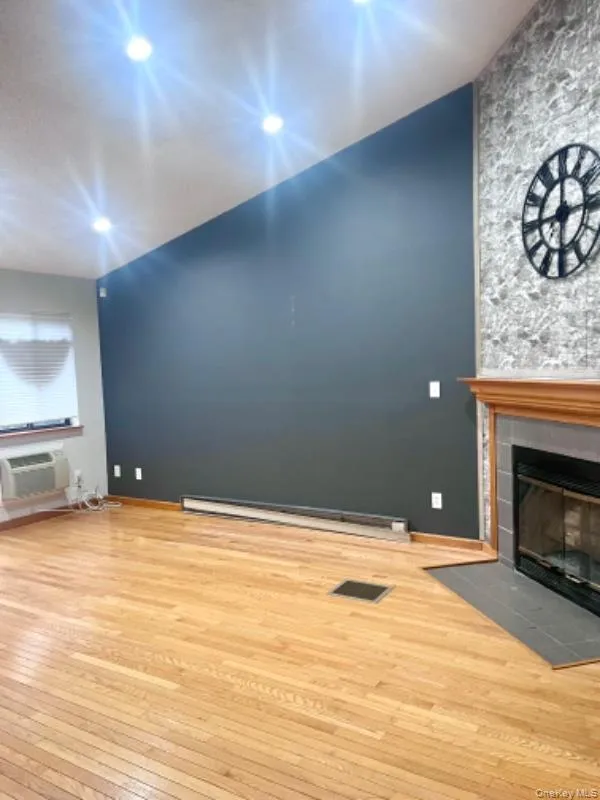 Unfurnished living room with hardwood / wood-style flooring, a baseboard radiator, and a fireplace Unfurnished living room with hardwood / wood-style flooring, a baseboard radiator, and a fireplace