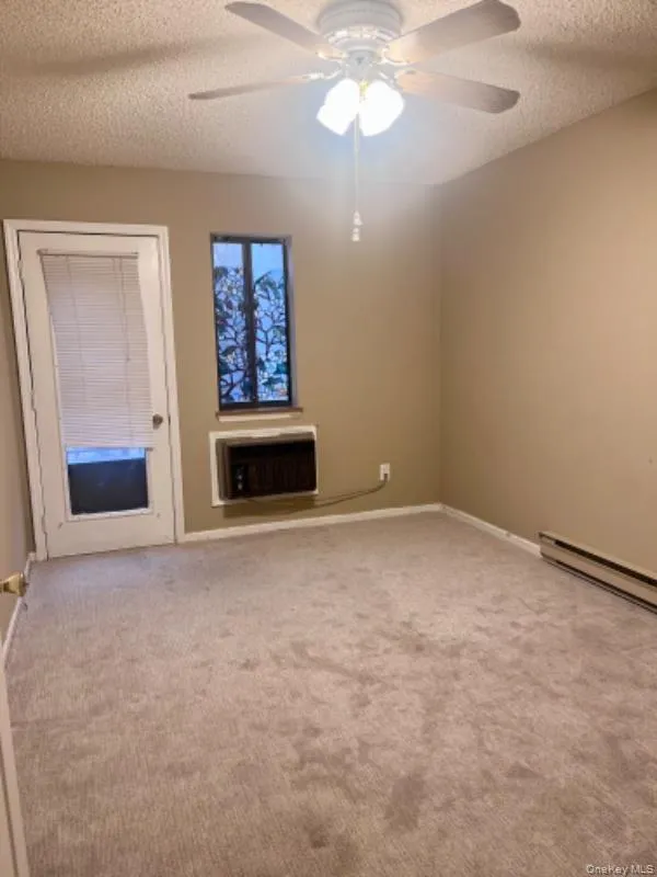 Empty room featuring a textured ceiling, light colored carpet, a baseboard radiator, heating unit, and a ceiling fan Empty room featuring a textured ceiling, light colored carpet, a baseboard radiator, heating unit, and a ceiling fan