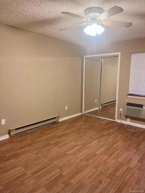 Unfurnished bedroom with baseboard heating, light wood-type flooring, a textured ceiling, a ceiling fan, and a closet Unfurnished bedroom with baseboard heating, light wood-type flooring, a textured ceiling, a ceiling fan, and a closet