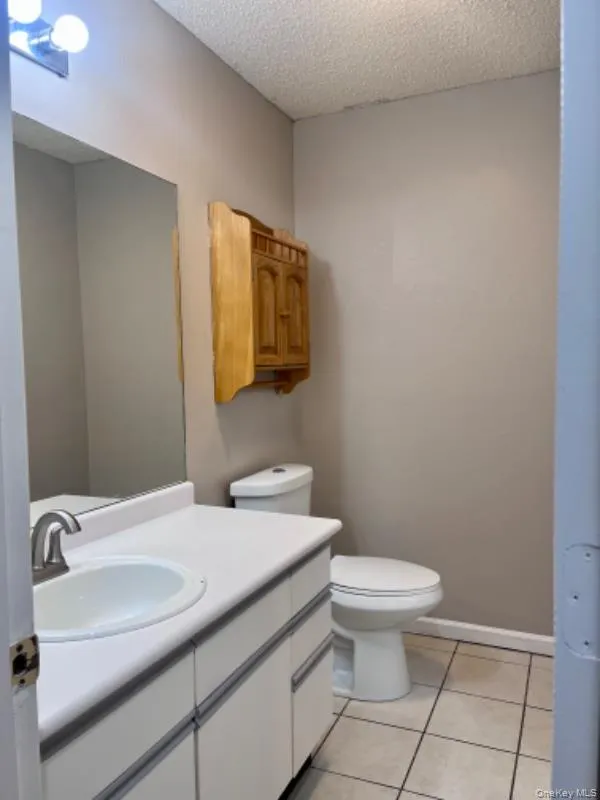 Half bathroom with light tile patterned floors, a textured ceiling, and vanity Half bathroom with light tile patterned floors, a textured ceiling, and vanity