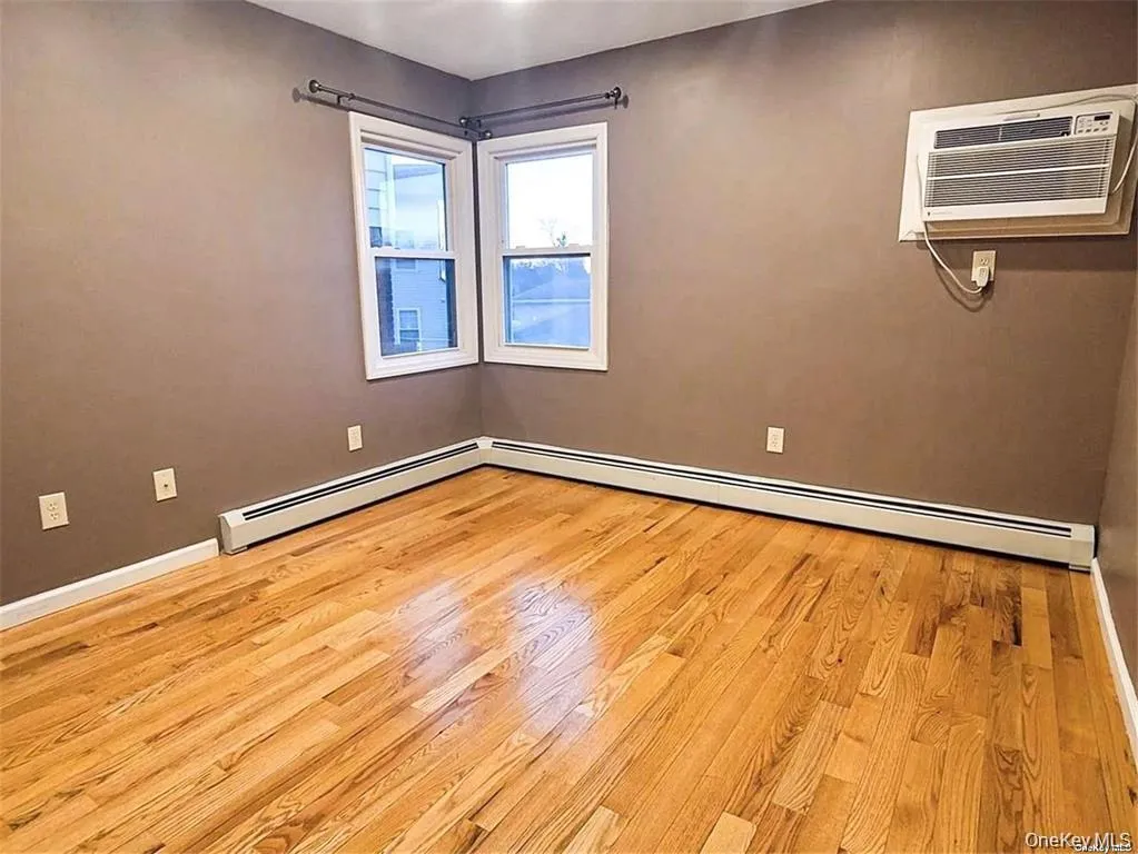 Unfurnished room featuring a baseboard heating unit, light wood finished floors, and an AC wall unit Unfurnished room featuring a baseboard heating unit, light wood finished floors, and an AC wall unit