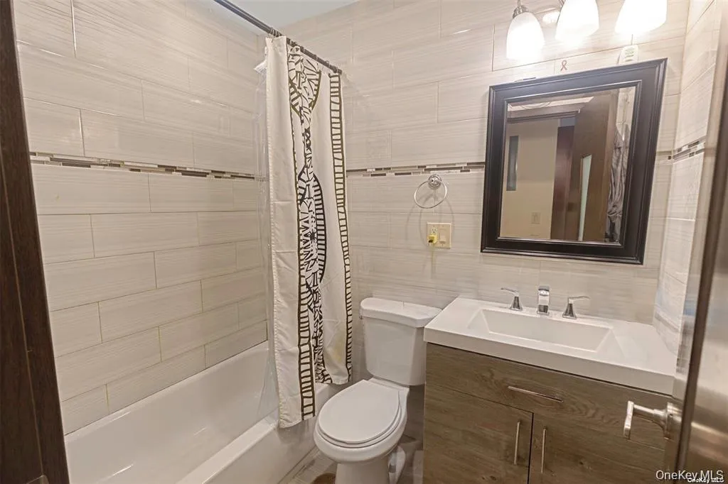 Bathroom featuring shower / tub combo with curtain, vanity, and tile walls Bathroom featuring shower / tub combo with curtain, vanity, and tile walls