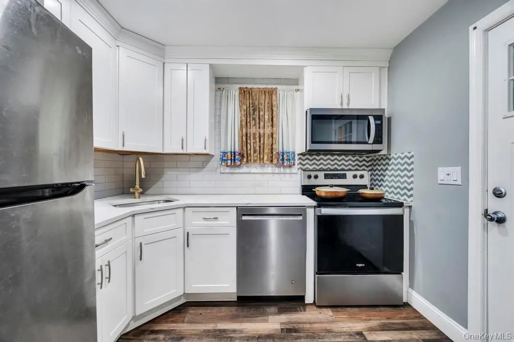 Kitchen featuring stainless steel appliances, white cabinetry, backsplash, and light stone countertops Kitchen featuring stainless steel appliances, white cabinetry, backsplash, and light stone countertops