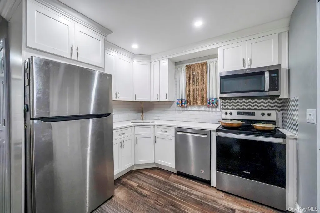 Kitchen featuring stainless steel appliances, white cabinetry, tasteful backsplash, dark wood-style flooring, and light stone counters Kitchen featuring stainless steel appliances, white cabinetry, tasteful backsplash, dark wood-style flooring, and light stone counters