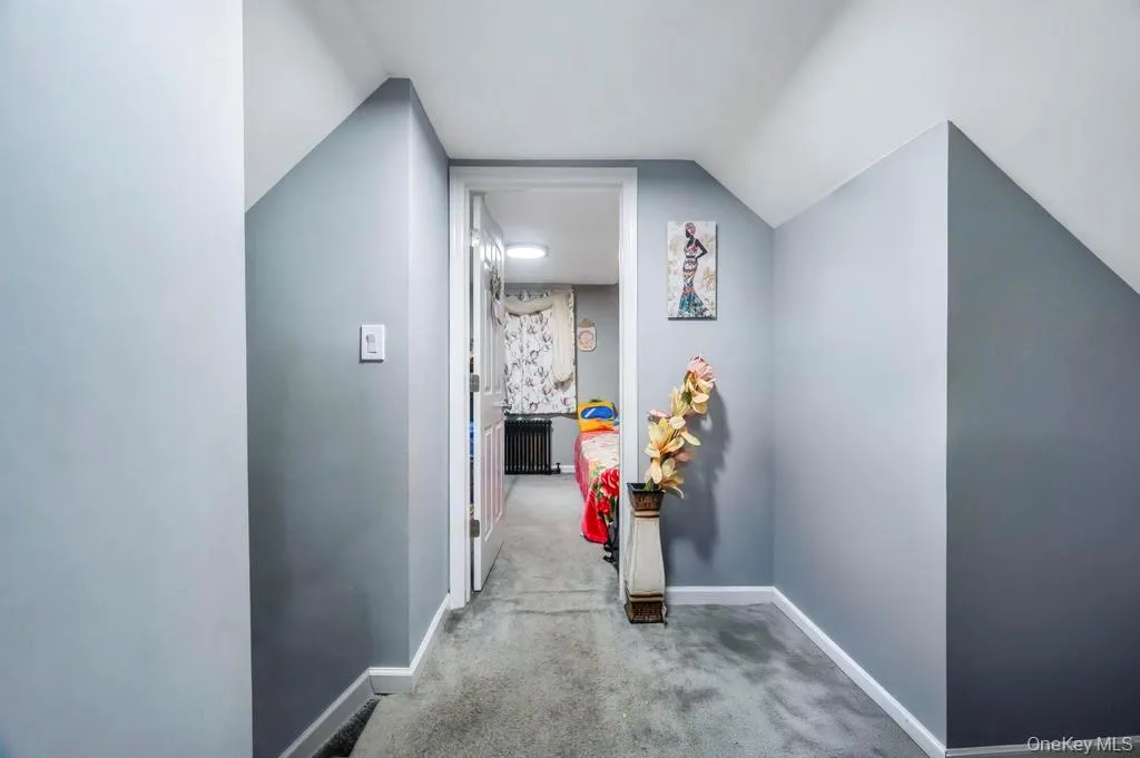 Corridor featuring carpet floors, radiator, and vaulted ceiling Corridor featuring carpet floors, radiator, and vaulted ceiling