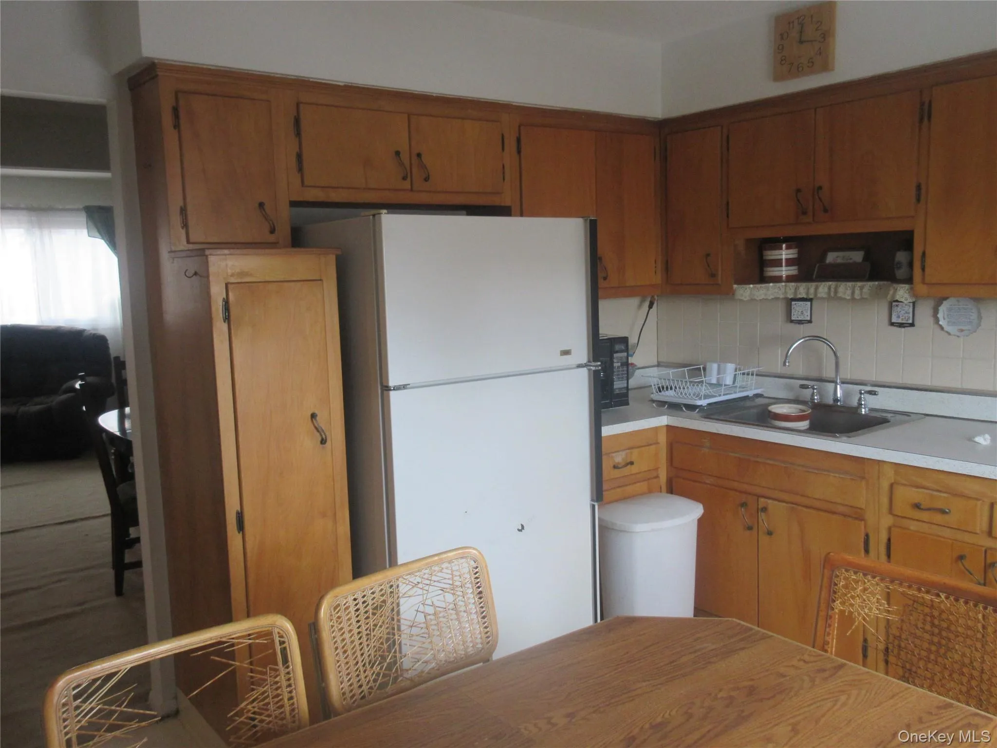 Kitchen featuring freestanding refrigerator, light countertops, brown cabinets, tasteful backsplash, and black microwave Kitchen featuring freestanding refrigerator, light countertops, brown cabinets, tasteful backsplash, and black microwave