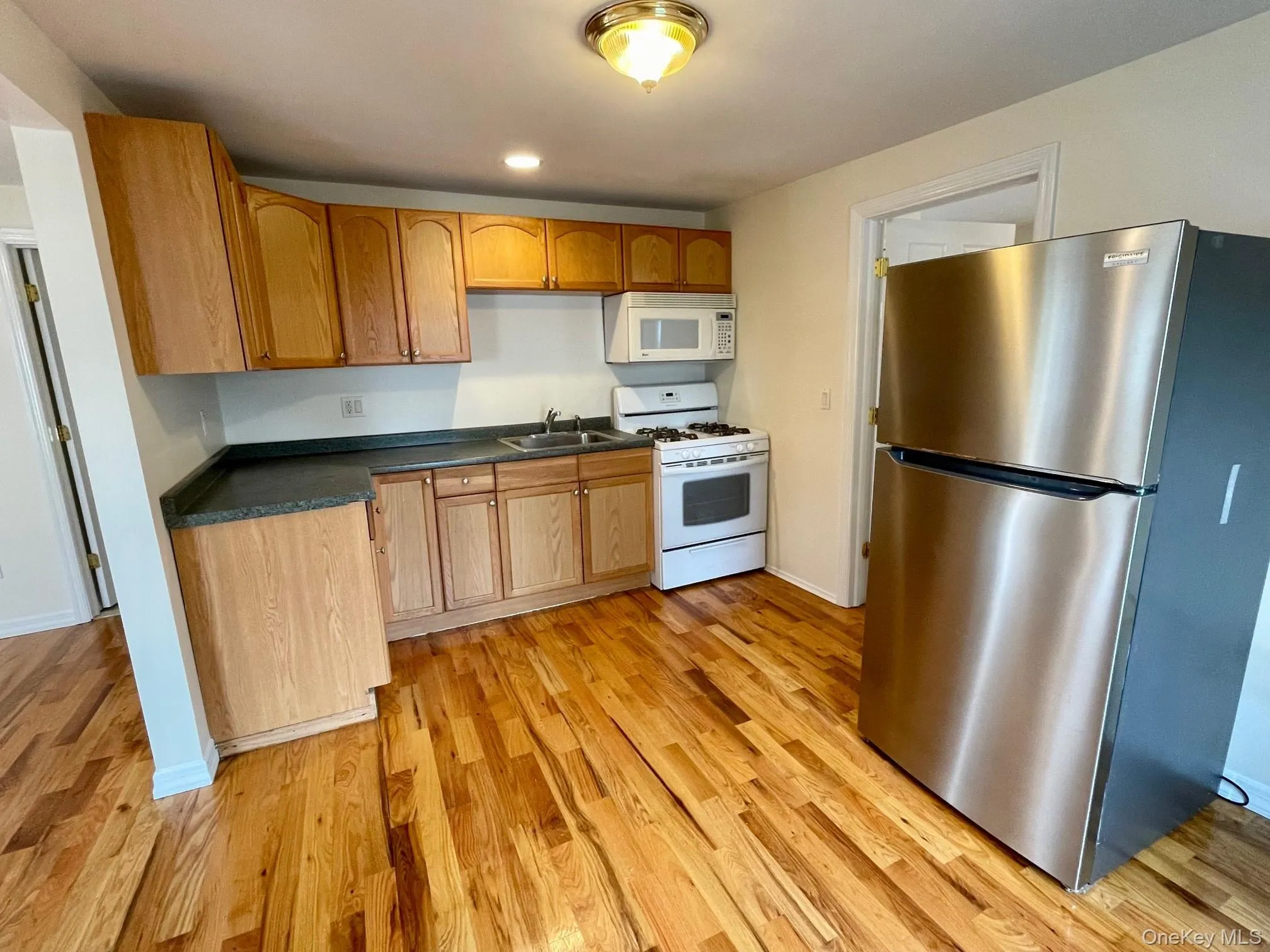 Kitchen with white appliances, dark countertops, and light wood finished floors Kitchen with white appliances, dark countertops, and light wood finished floors