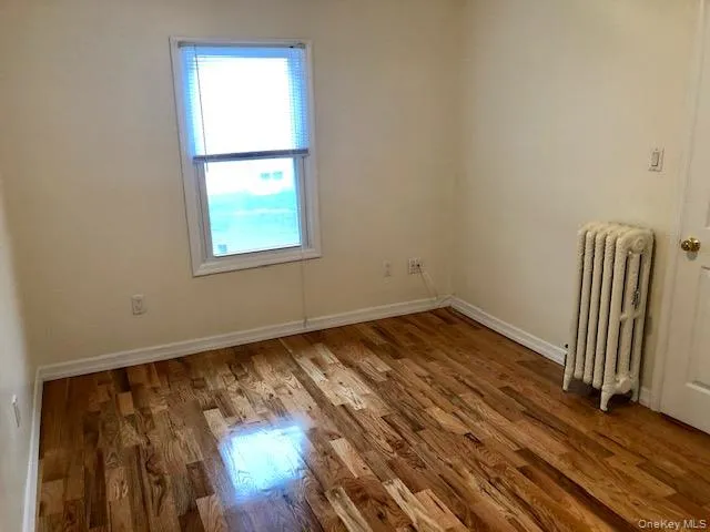 Spare room featuring radiator and wood finished floors Spare room featuring radiator and wood finished floors