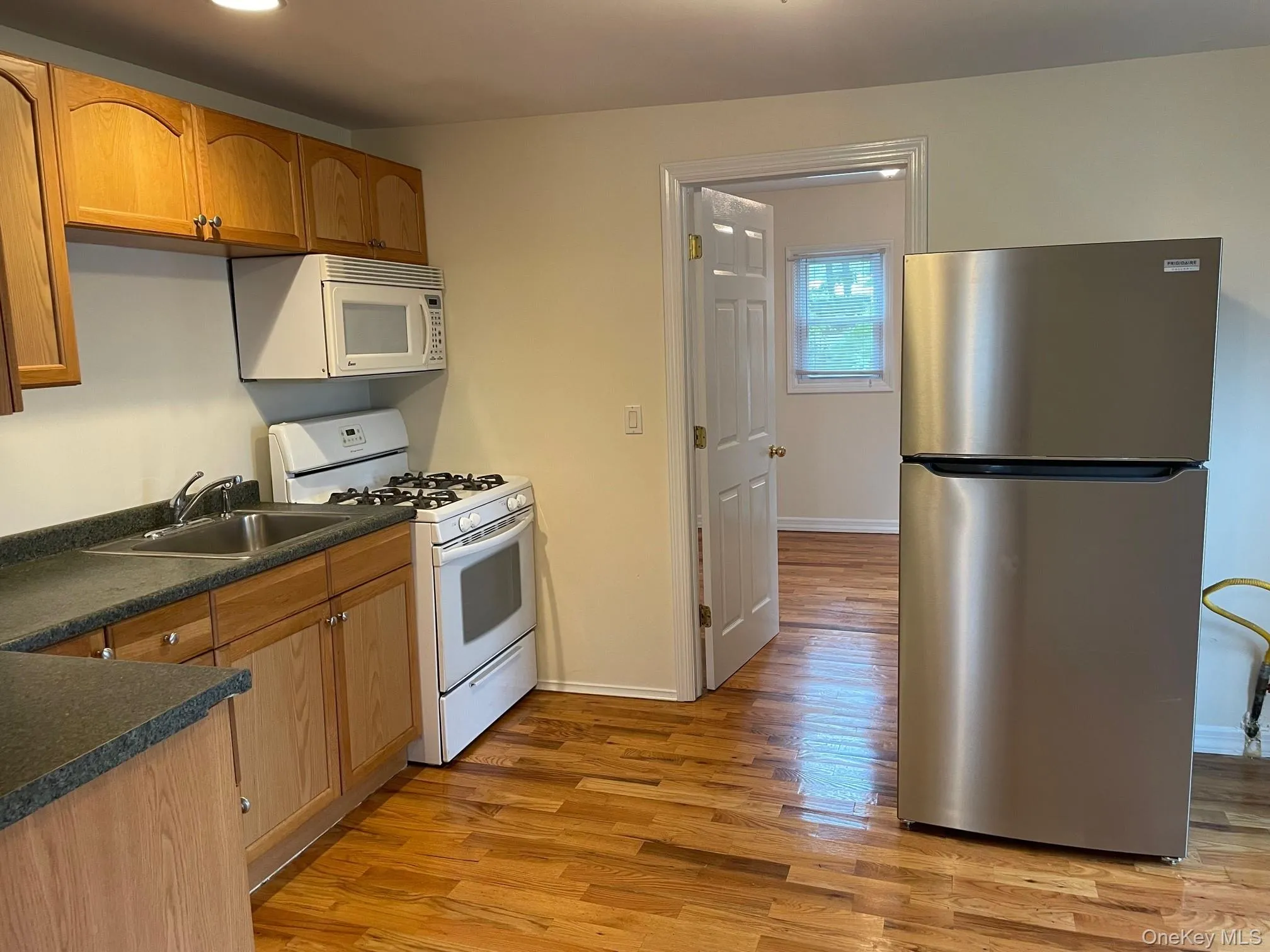 Kitchen featuring white appliances, dark countertops, light wood finished floors, and brown cabinetry Kitchen featuring white appliances, dark countertops, light wood finished floors, and brown cabinetry