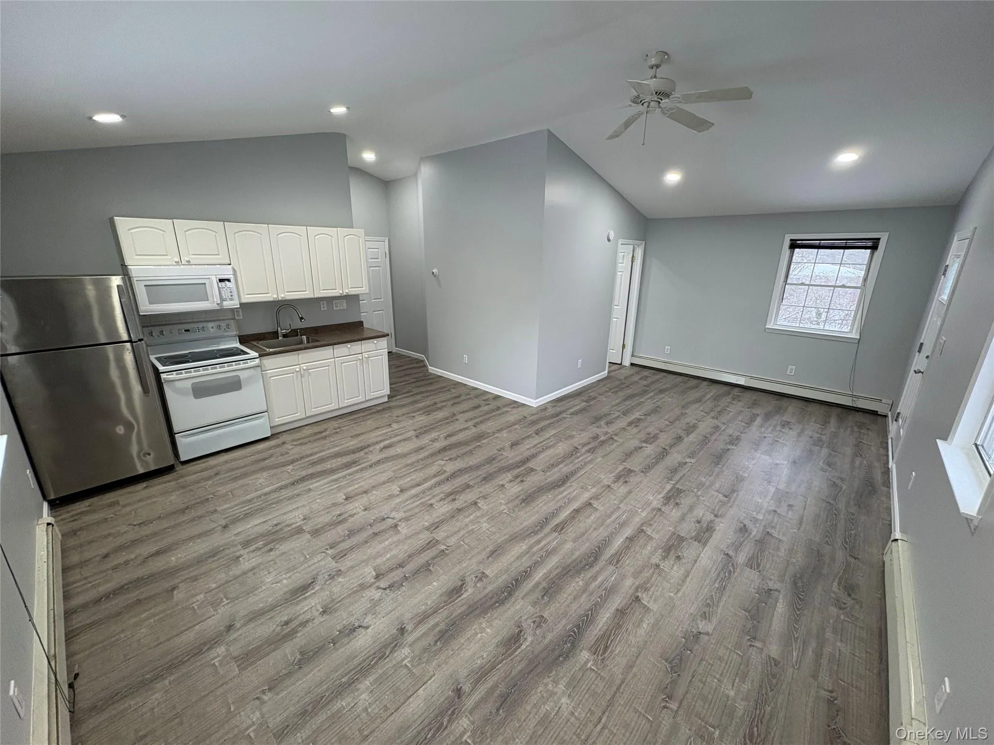 Kitchen with white appliances, white cabinets, dark countertops, light wood-type flooring, and vaulted ceiling Kitchen with white appliances, white cabinets, dark countertops, light wood-type flooring, and vaulted ceiling